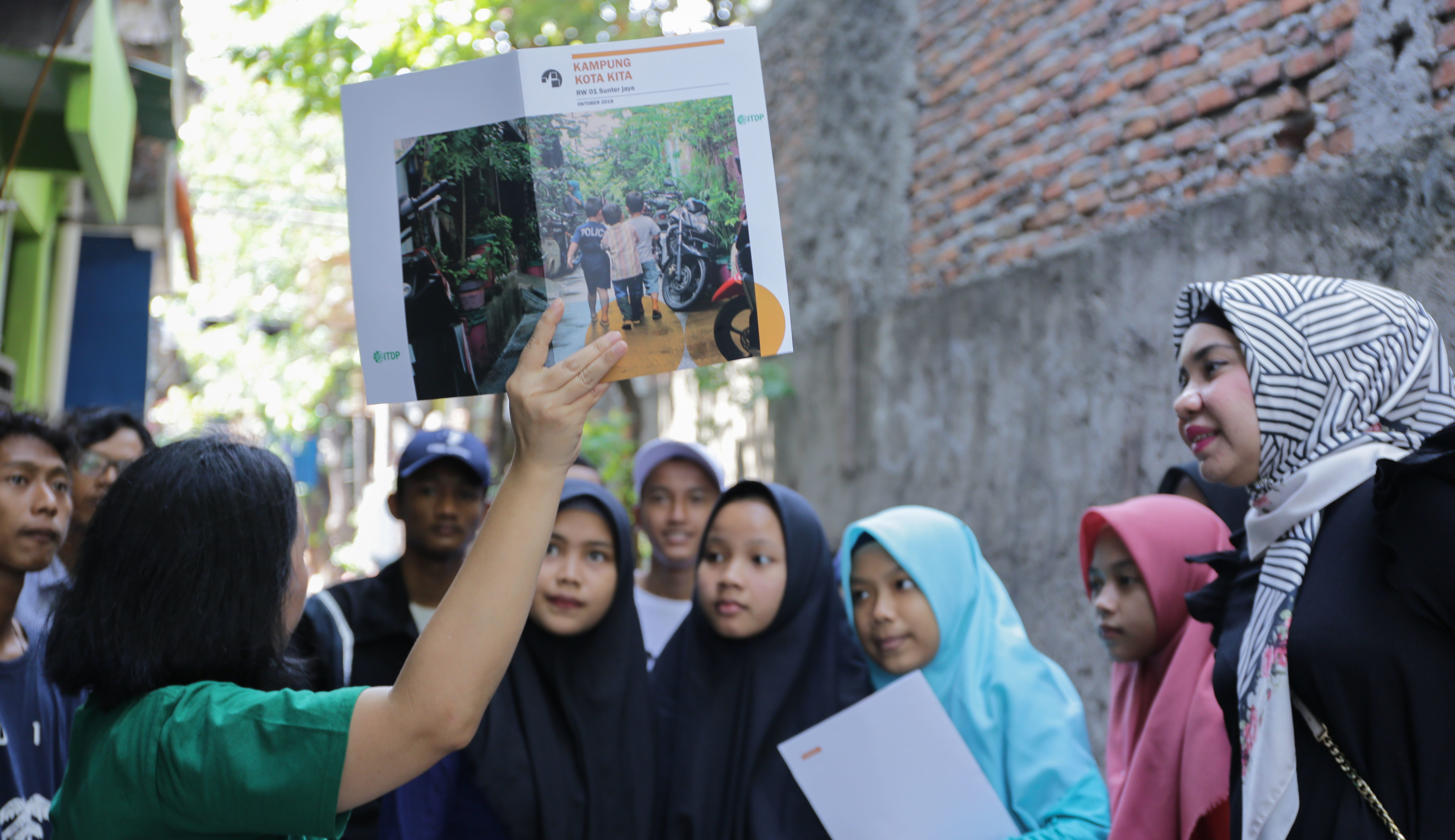 woman holding up ITDP Indonesia publication in front of group of women and girls