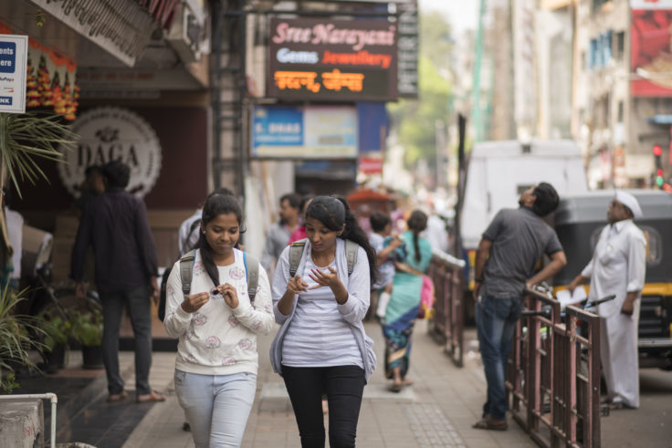 Girls on phones walking along sidewalk in Pune, India