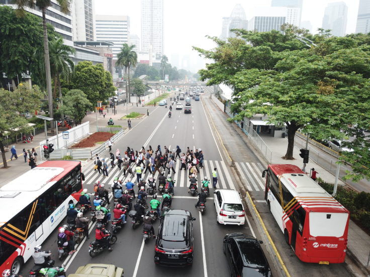Two buses, many cars, and multiple motorcycles at a crosswalk in Jakarta