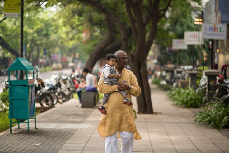 Man holds small child while walking along sidewalks in Pune, India