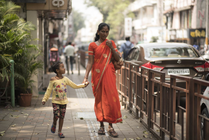 Woman in orange sari walks with child along pedestrian footpath