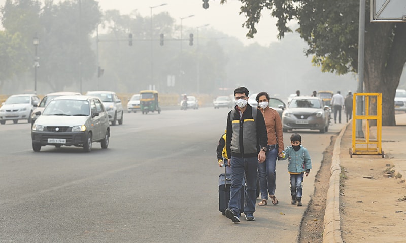 Family of four wearing dust masks walks along non sidewalk next to speeding cars in India
