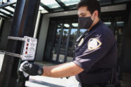 Man in dark mask and gloves sanitizing a pedestrian crosswalk button