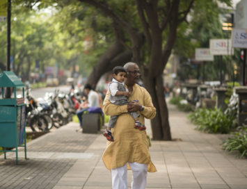 Elderly man carrying a baby boy as he walks down the street in Pune